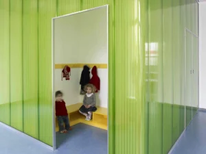 Kleine Garderobennische für Kinder com integrierten gelben Sitzbänken und Kleiderhaken, gerahmt von einer gewellten grünen Trennwand.