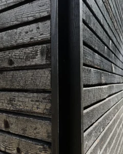 Nahaufnahme der Textur einer karbonisierten Holzfassade, die a die traditionelle verbrannte Holzoberfläche an einer architektonischen Eckverbindung zeigt.