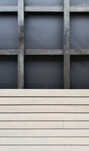 Architektonisches Detail einer nachhaltigen Holzfassade im Bau, das horizontale Holzverkleidungslamellen über einer schwarzen Dämmschicht zeigt.