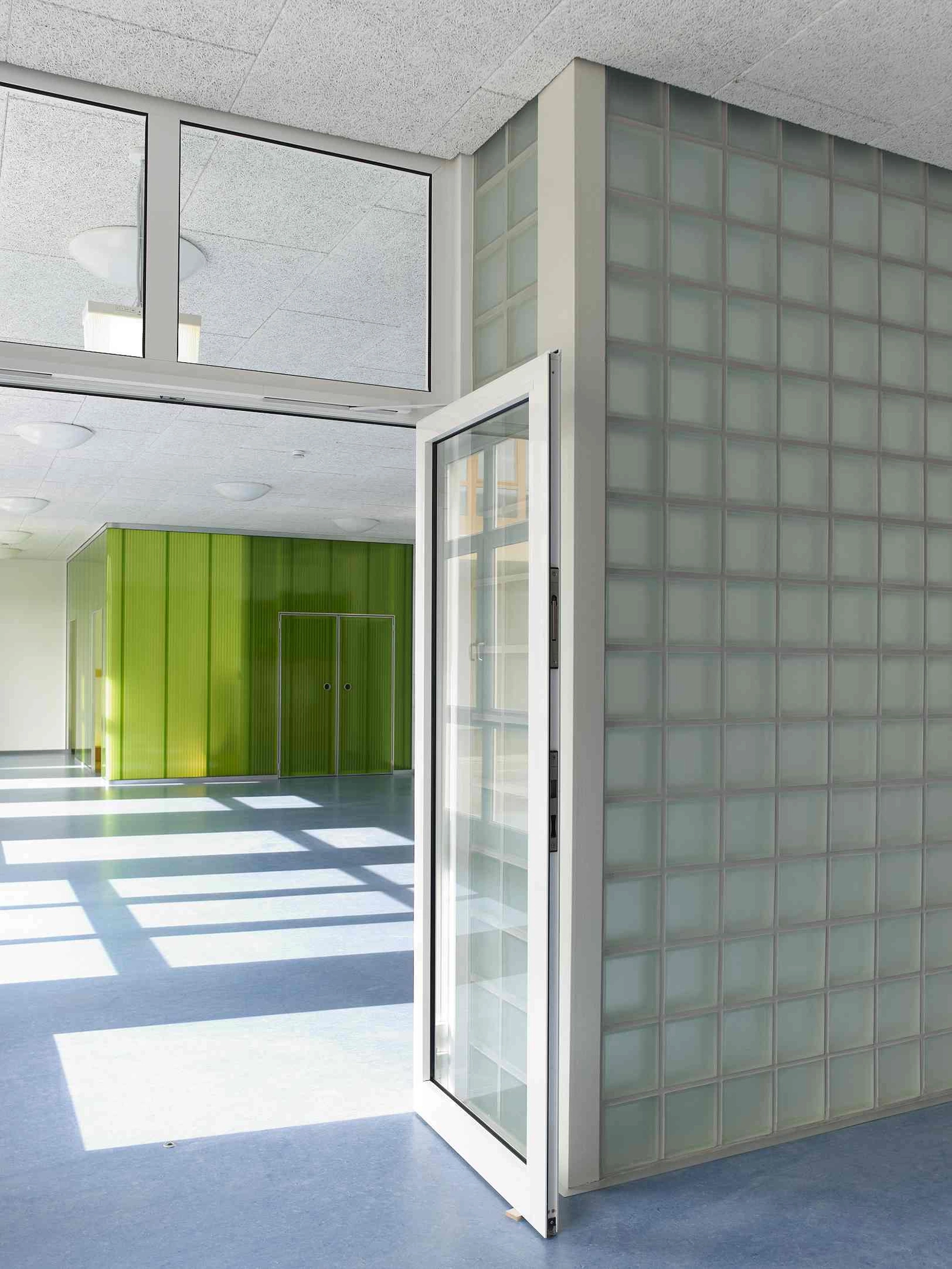 EN_United-Architektur-Haus-des-Kindes-Nursery-school-Verbindung Interior view of an educational facility showing a white door frame next to a matte glass block wall, with green panels visible in the background.