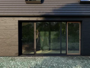 Modern residential building facade with horizontal dark siding, large glass sliding doors reflecting the forest, and a rustic cobblestone patio.