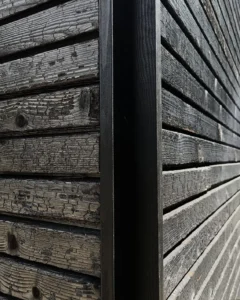 Close-up texture of a charred wood facade showing the traditional carbonized timber texture on an architectural corner joint.