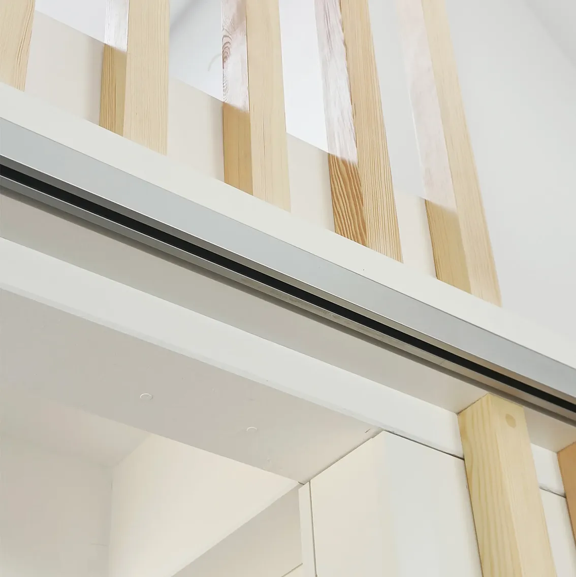 EN_United-Architektur-House-Uckermark-Lakes-Nature-Park-Sliding-Door Architectural close-up of custom interior carpentry featuring light wood slats, integrated sliding door tracks, and minimalist white finishes.
