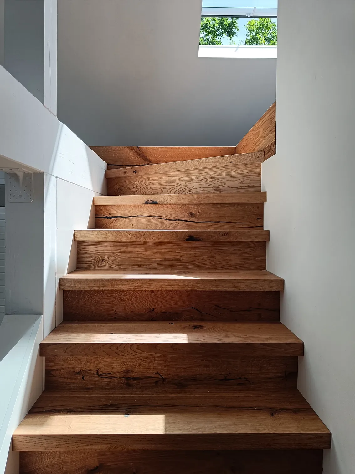 EN_United-Architektur-House-Uckermark-Lakes-Nature-Park-Stairs Modern solid oak staircase with natural wood grain, illuminated by soft natural light from a skylight window above.