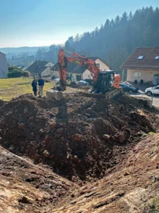 Ground preparation and earthworks on a steep residential plot, featuring an orange excavator digging the foundation on a hillside terrain.