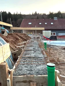 Construction site progress showing concrete pouring for a strip foundation with steel reinforcement mesh on a residential plot.