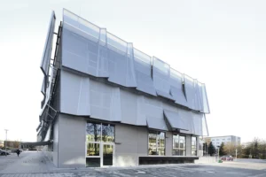Exterior perspective of a contemporary office structure highlighting its geometric, overlapping mesh facade screens and large ground-floor windows.