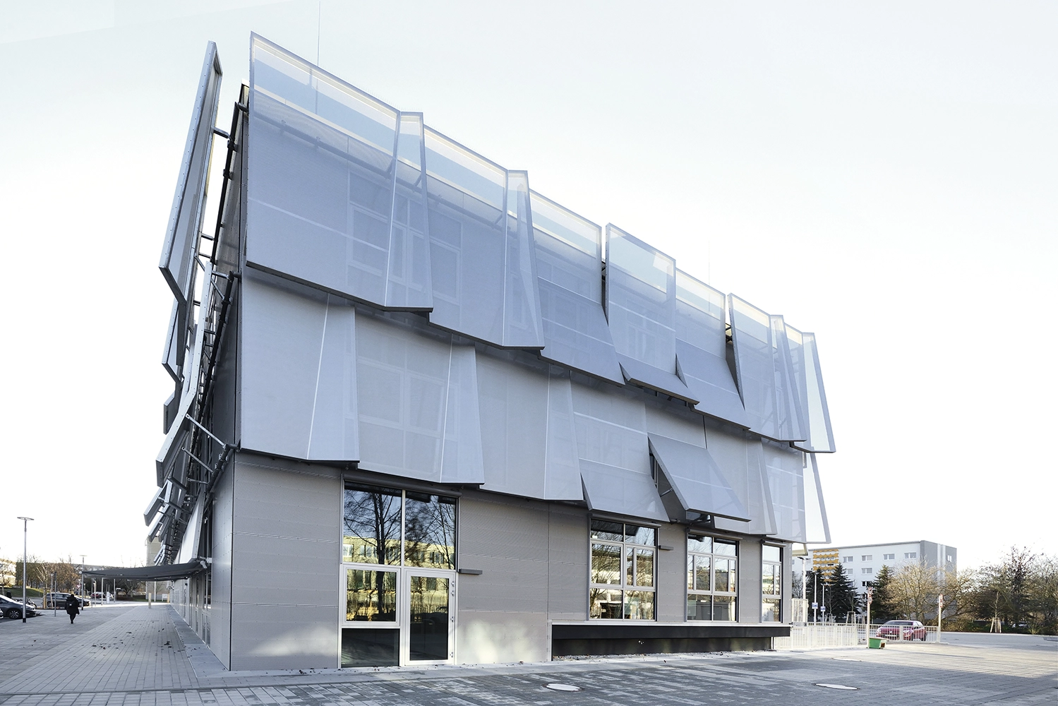 Exterior perspective of a contemporary office structure highlighting its geometric, overlapping mesh facade screens and large ground-floor windows.