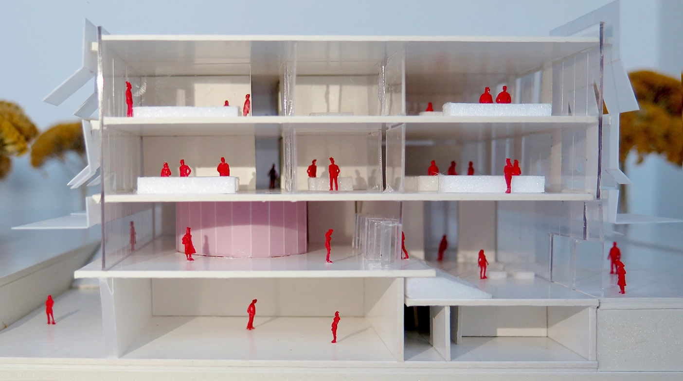 Cross-section view of an architectural scale model exposing four office floors with miniature red scale figures, interior partitions, and a central pink cylindrical core.
